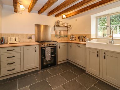 A kitchen with wooden beams on the ceiling cabinets a stove a toaster and a window at 1 White House Cottages Bromsash near Lea