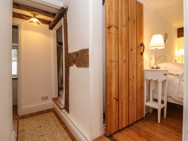 A hallway with wooden beams leading to a bedroom with a wooden door a white bedside table and a lamp at 1 White House Cottages Bromsash near Lea