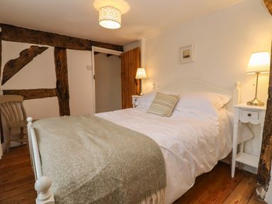 A bedroom with a bed side tables lamps and a chair at 1 White House Cottages in Bromsash near Lea