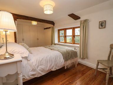 A bedroom with a bed a nightstand lamp a window with curtains a wooden chair and built in wardrobes at 1 White House Cottages Bromsash near Lea