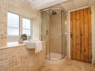 A bathroom with a corner shower enclosure a sink with a towel frosted window and wooden door at 1 White House Cottages in Bromsash near Lea