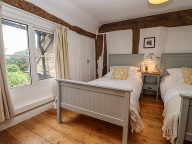 A bedroom with two single beds a bedside table lamp and a window with curtains at 1 White House Cottages Bromsash near Lea