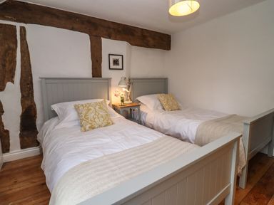 A bedroom with two single beds a bedside table with a lamp and flowers and exposed wooden beams at 1 White House Cottages Bromsash near Lea