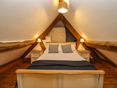 A bedroom with a bed between two nightstands under a pitched ceiling with exposed wooden beams at 1 White House Cottages Bromsash near Lea