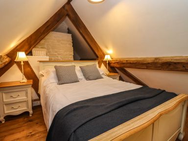 A bedroom with a large bed, two bedside tables with lamps, wooden beams, and a sloped ceiling at 1 White House Cottages Bromsash near Lea