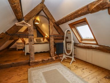 An attic bedroom with wooden beams a bed a bedside table a standing mirror and a skylight window at 1 White House Cottages Bromsash near Lea