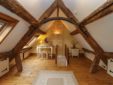 An attic room with wooden beams a dressing table a stool a lamp and a small drawer unit at 1 White House Cottages Bromsash near Lea