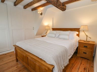 A bedroom with a wooden bed frame two pillows two bedside tables with lamps and wooden beams on the ceiling at 1 White House Cottages Bromsash near Lea