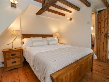A bedroom with a wooden double bed two bedside tables with lamps exposed wooden ceiling beams and a wooden floor at 1 White House Cottages Bromsash near Lea