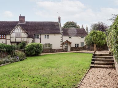 A garden with grass lawn and gravel path in front of a traditional cottage at 1 White House Cottages Bromsash near Lea