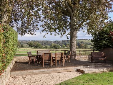 A wooden patio set with chairs and a bench under a tree in a garden with countryside views at 1 White House Cottages in Bromsash near Lea