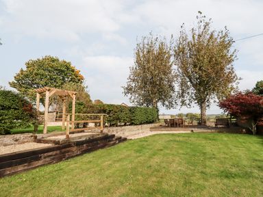 A garden with grass trees hedge a wooden pergola and a seating area with table and chairs at 1 White House Cottages Bromsash near Lea