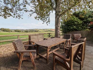 An outdoor wooden table and chairs set on a wooden deck under a tree overlooking fields at 1 White House Cottages in Bromsash near Lea