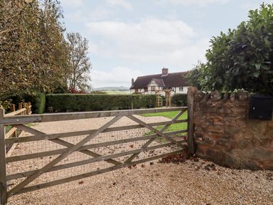 A wooden gate leading to a gravel driveway with a house and garden in the background at 1 White House Cottages Bromsash near Lea