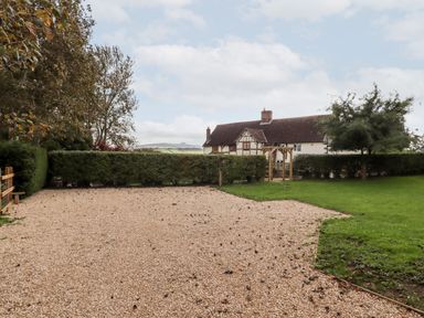 A gravel driveway with a grassy area and hedges in front of a traditional house at 1 White House Cottages in Bromsash near Lea