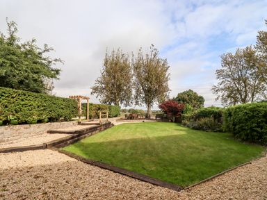 A garden with green lawn gravel paths trees hedges and outdoor seating at 1 White House Cottages Bromsash near Lea