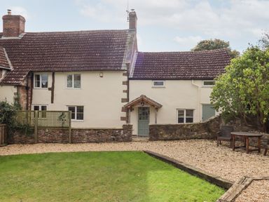 Exterior view of a two section cream colored house with a tiled roof a green front door a small patio area with wooden chairs and table and a green lawn at 1 White House Cottages Bromsash near Lea