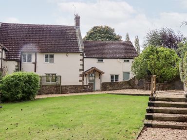 A cottage with a tiled roof a lawn a bush and outdoor seating at 1 White House Cottages Bromsash near Lea