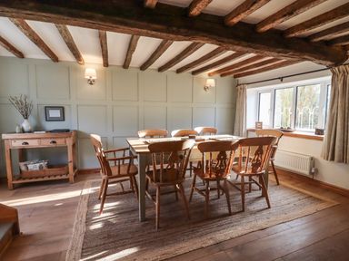 A dining room with wooden table and chairs under ceiling beams at 1 White House Cottages Bromsash near Lea
