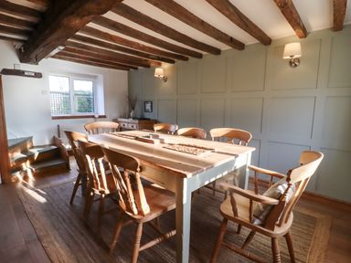 A dining room with wooden table and chairs exposed beams and a window at 1 White House Cottages Bromsash near Lea