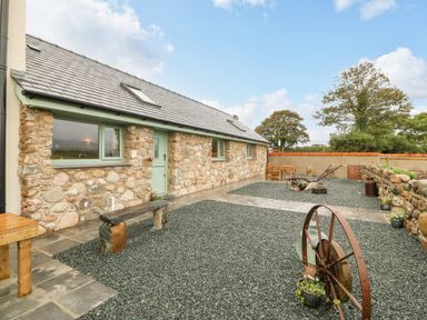 An exterior view of a stone house with green window frames and door a gravel yard with rustic bench and metal wheel at Y Felin The Granary in Caernarfon