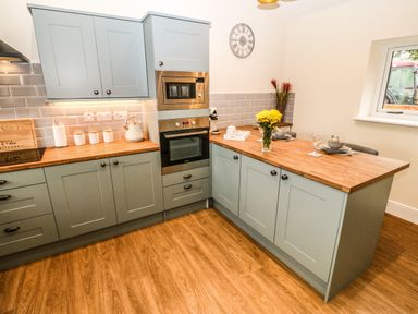 A kitchen with gray cabinets wooden countertops a built-in oven and microwave a clock yellow flowers and table settings at Y Felin The Granary in Caernarfon