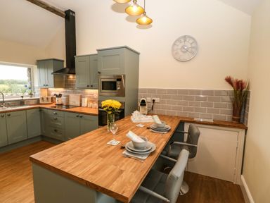 A kitchen with green cabinets wooden countertops a dining bar set for two and appliances at Y Felin The Granary in Caernarfon