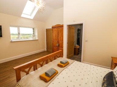 A bedroom with a wooden bed and wardrobe near a window and an open door showing a bathroom at Y Felin The Granary in Caernarfon