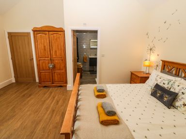 A bedroom with a wooden bed and wardrobe towels on the bed and a door leading to a bathroom at Y Felin The Granary in Caernarfon