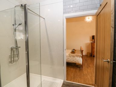 A bathroom with a glass shower enclosure and a view into a bedroom with a wooden bed and dresser at Y Felin The Granary in Caernarfon