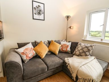 A corner sofa with cushions and a blanket next to a window in a living room at Ty Gwair The Hayloft in Caernarfon