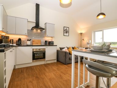 A kitchen and dining area with a gray sofa and modern appliances at Ty Gwair (The Hayloft) in Caernarfon