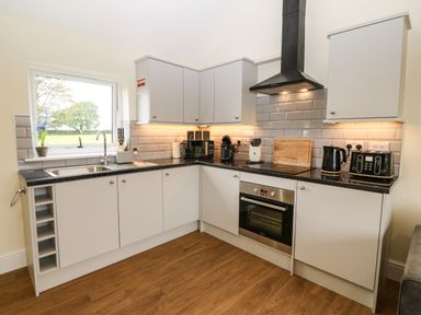A kitchen with white cabinets a black countertop an oven a toaster a kettle and a window at Ty Gwair The Hayloft in Caernarfon