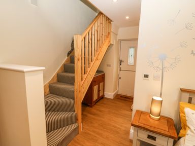 A hallway with a wooden staircase carpeted in stripes and a small wooden cabinet near the front door at Ty Gwair The Hayloft in Caernarfon