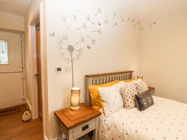 A bedroom with a bed next to wooden nightstands and a door in the corner at Ty Gwair The Hayloft in Caernarfon