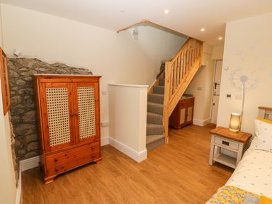 A bedroom with wooden furniture a striped carpeted staircase and a bed with a bedside table and lamp at Ty Gwair The Hayloft in Caernarfon