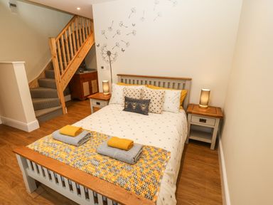 A bedroom with a bed two bedside tables with lamps and a staircase at Ty Gwair The Hayloft in Caernarfon