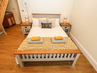 A bedroom with a wooden bed with gray and white bedding and two bedside tables with lamps at Ty Gwair The Hayloft in Caernarfon