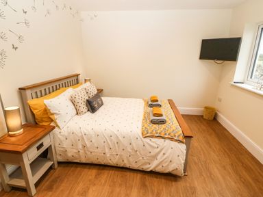 A bedroom with a bed and side table with lamps a wall mounted TV and a window at Ty Gwair The Hayloft in Caernarfon