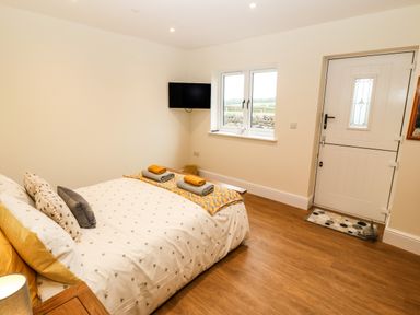 A bedroom with a double bed with pillows and folded towels a wall-mounted tv a window and a white door at Ty Gwair The Hayloft in Caernarfon
