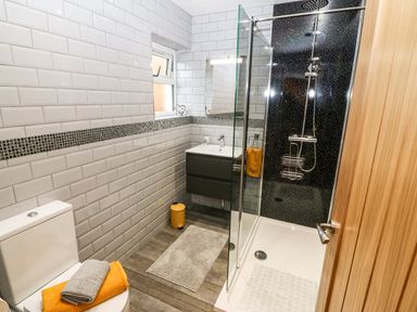 A bathroom with a toilet, sink, shower, towels, and a small window at Ty Gwair The Hayloft in Caernarfon