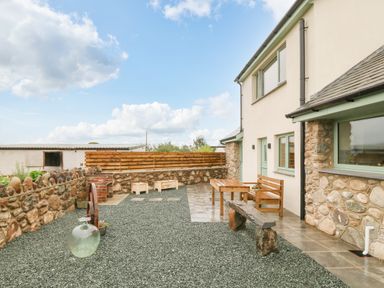 An outdoor patio area with wooden bench and table stone walls and gravel ground at Ty Gwair The Hayloft in Caernarfon