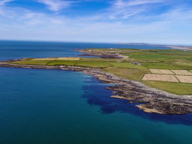 A coastal landscape with fields and rocky shoreline at 7 Bro Branwen in Aberffraw near Rhosneigr