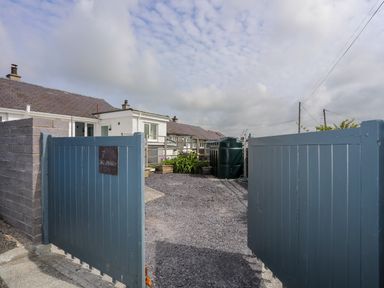 A driveway with blue wooden gates leading to a white house with a gravel yard at 7 Bro Branwen Aberffraw near Rhosneigr
