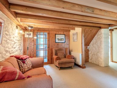A sitting room with a sofa, an armchair, wooden ceiling beams, and a stone wall at Tryfan Cottage in Rhostryfan near Caernarfon