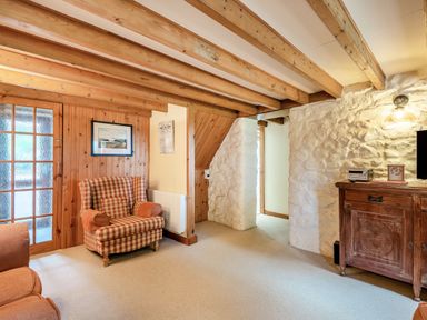 A living room with wooden beams on the ceiling a plaid armchair a wooden cabinet and stone walls at Tryfan Cottage in Rhostryfan near Caernarfon