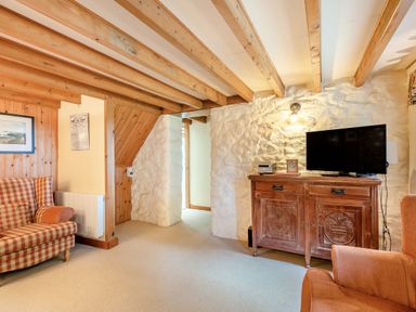 A living room with exposed wooden beams a wooden cabinet with a television and a checked armchair at Tryfan Cottage in Rhostryfan near Caernarfon