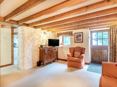 A living room with wooden beams a wooden door armchairs a television on a wooden cabinet and a window at Tryfan Cottage in Rhostryfan near Caernarfon
