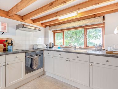 A kitchen with white cabinets gray countertops wooden ceiling beams a window over the sink and various kitchen appliances at Tryfan Cottage in Rhostryfan near Caernarfon
