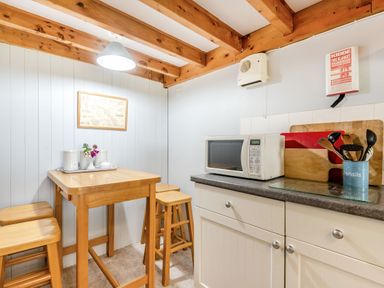 A small kitchen area with a wooden table and stools a microwave on a countertop and utensils in a container at Tryfan Cottage in Rhostryfan near Caernarfon